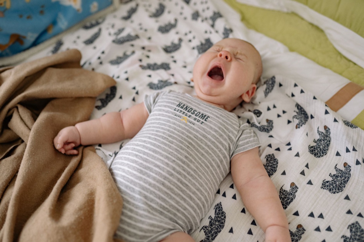 嬰兒穿白棉 Onesie 依偎在白 crib 中