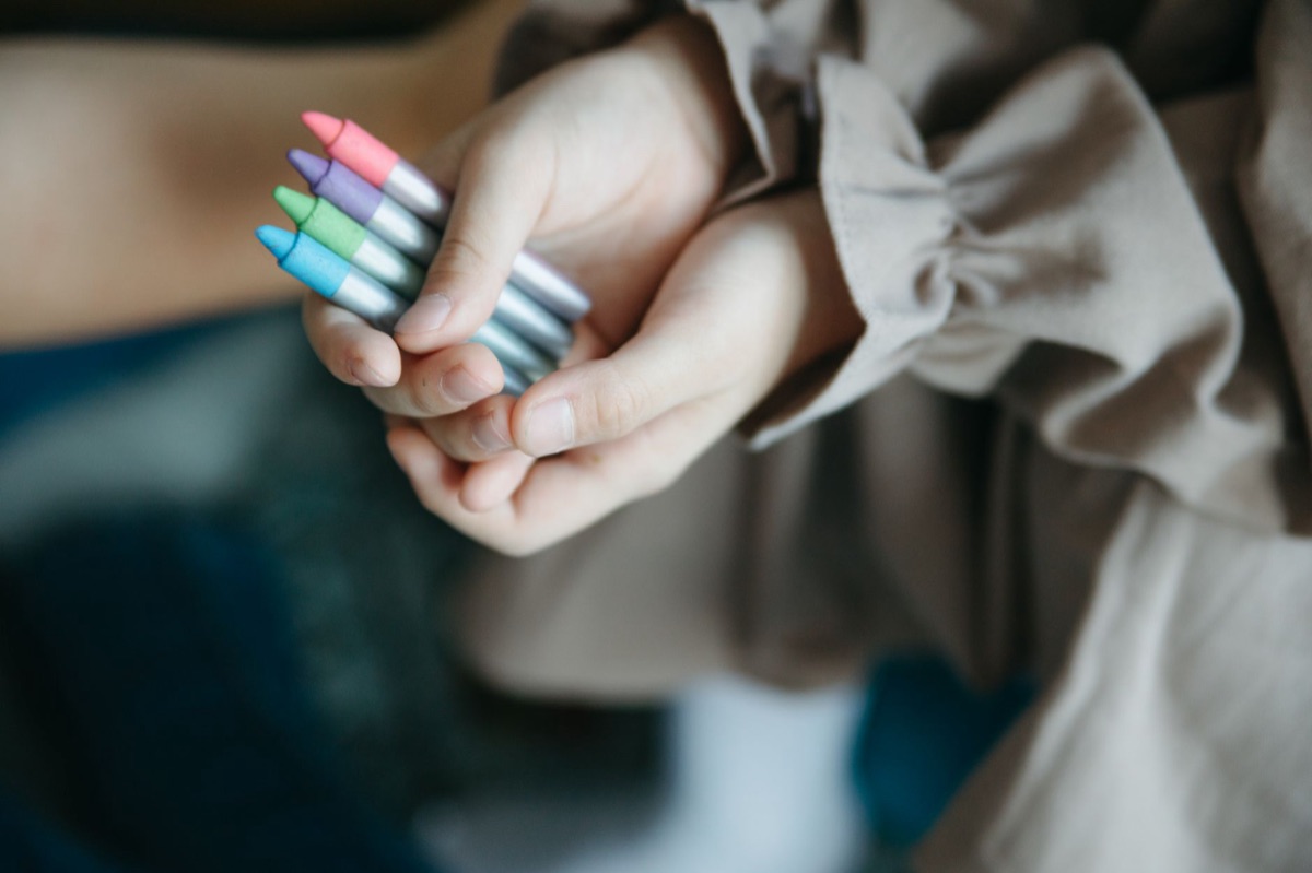 A child's hand using bright crayons to draw on white paper.