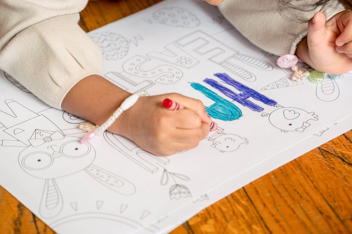 Criança desenhando com giz de cera em um papel.